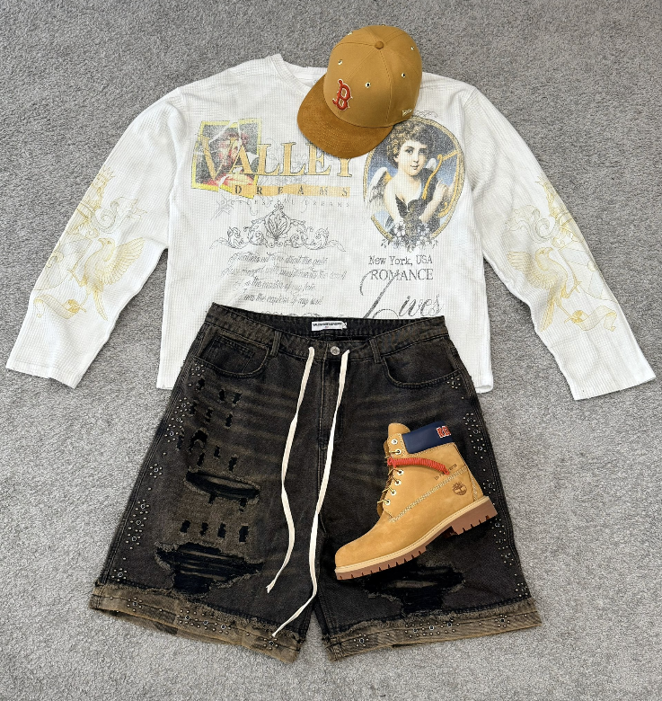 Look con camiseta blanca de manga larga estampada, bermuda negra, gorra mostaza y bota color trigo.