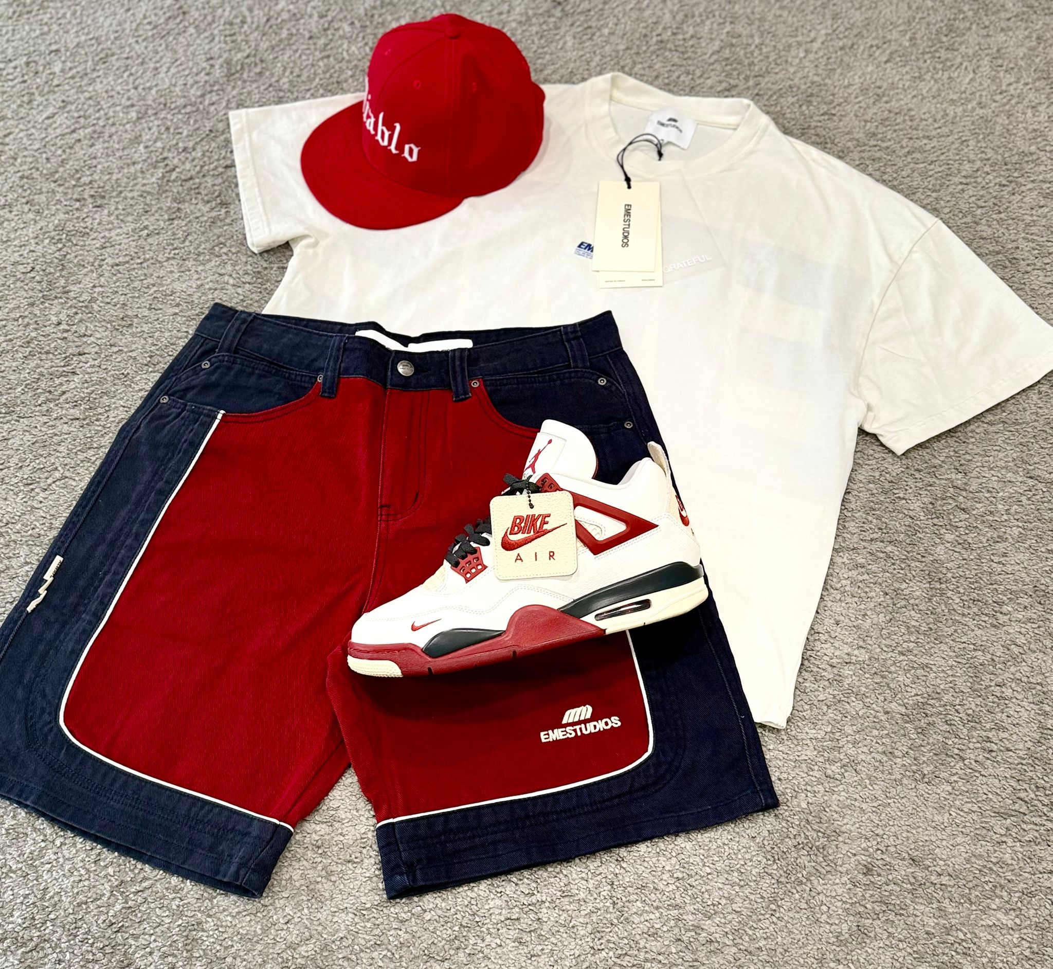 Look con camiseta blanca, bermuda roja y azul oscuro, gorra roja y zapatilla blanca con detalles rojos.