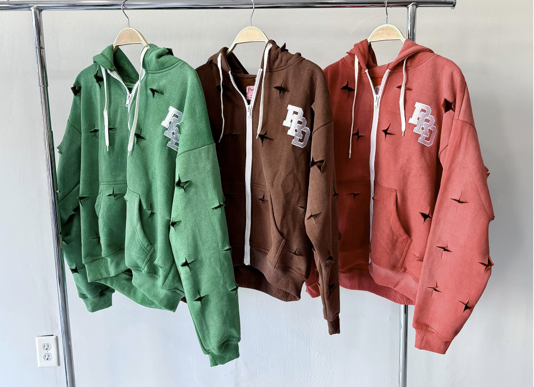 Tres sudaderas con capucha y cierre, en verde, marrón y coral, con detalles recortados.